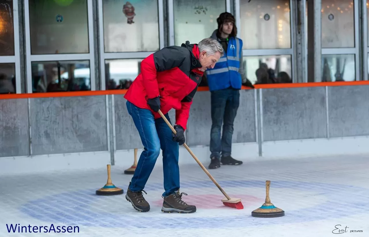 Een man in een rode jas veegt het ijs voor een curlingsteen