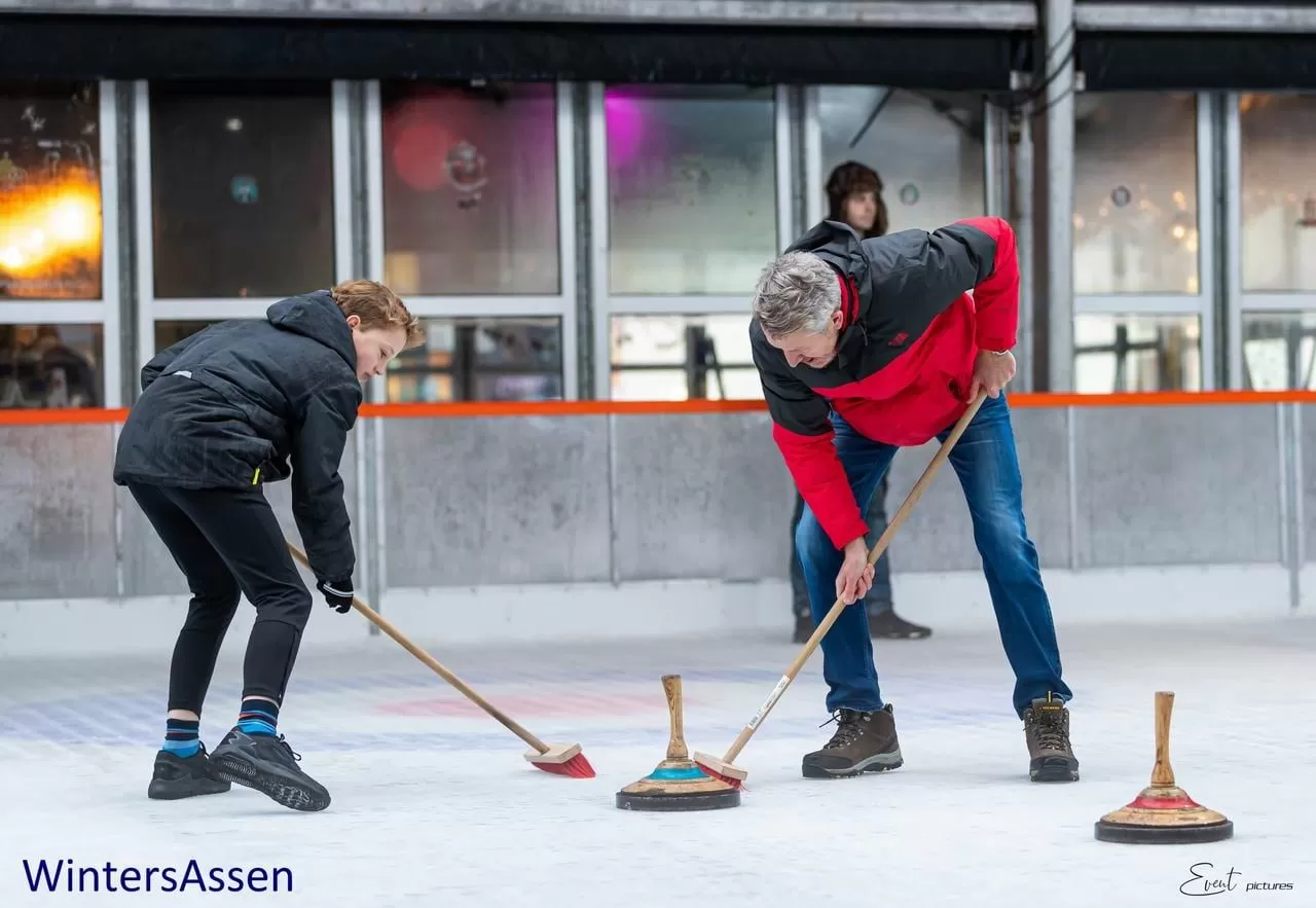 Twee curlingspelers vegen het ijs voor een curlingsteen