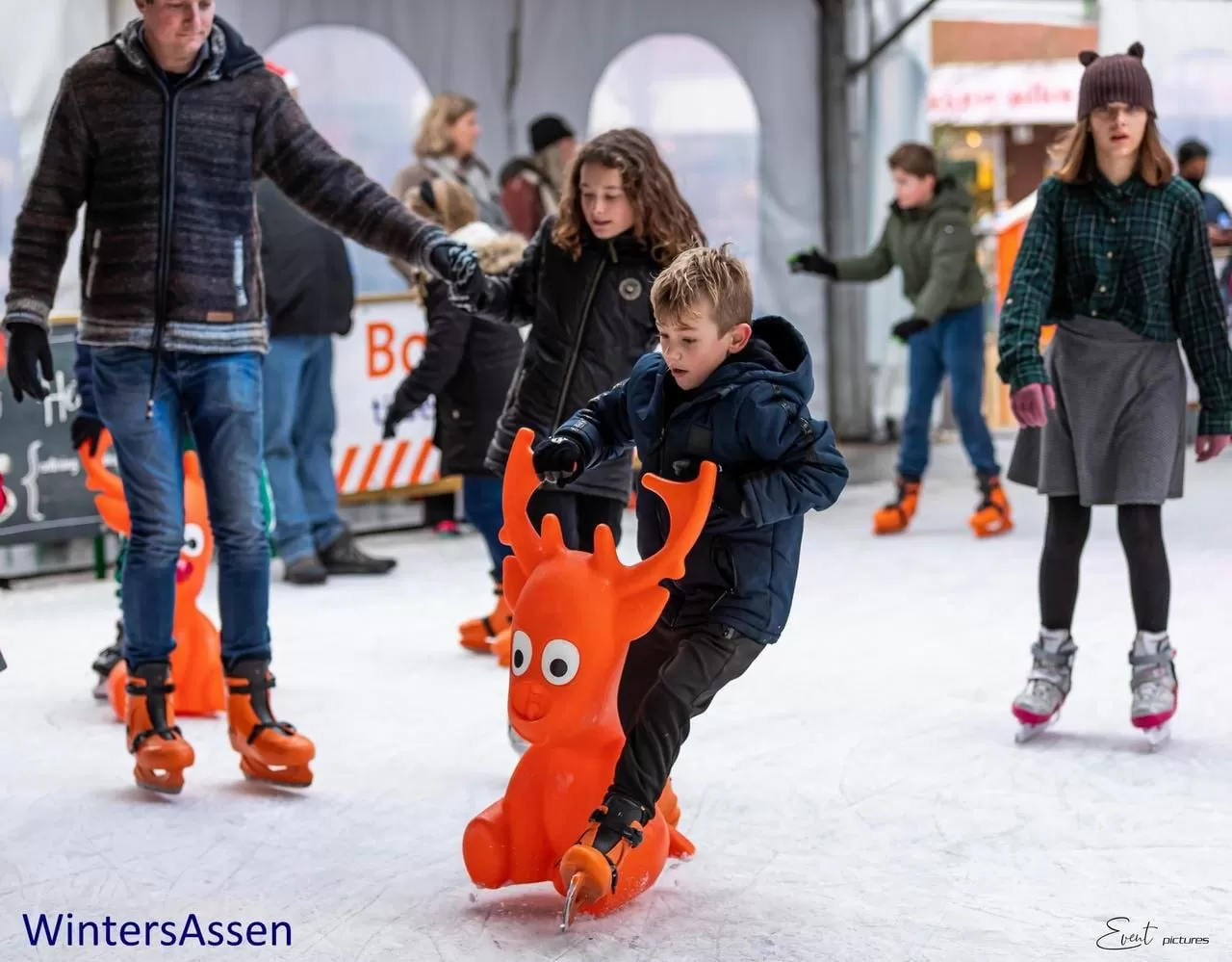 Een kind schaatst met een oranje zeehond als schaatshulp